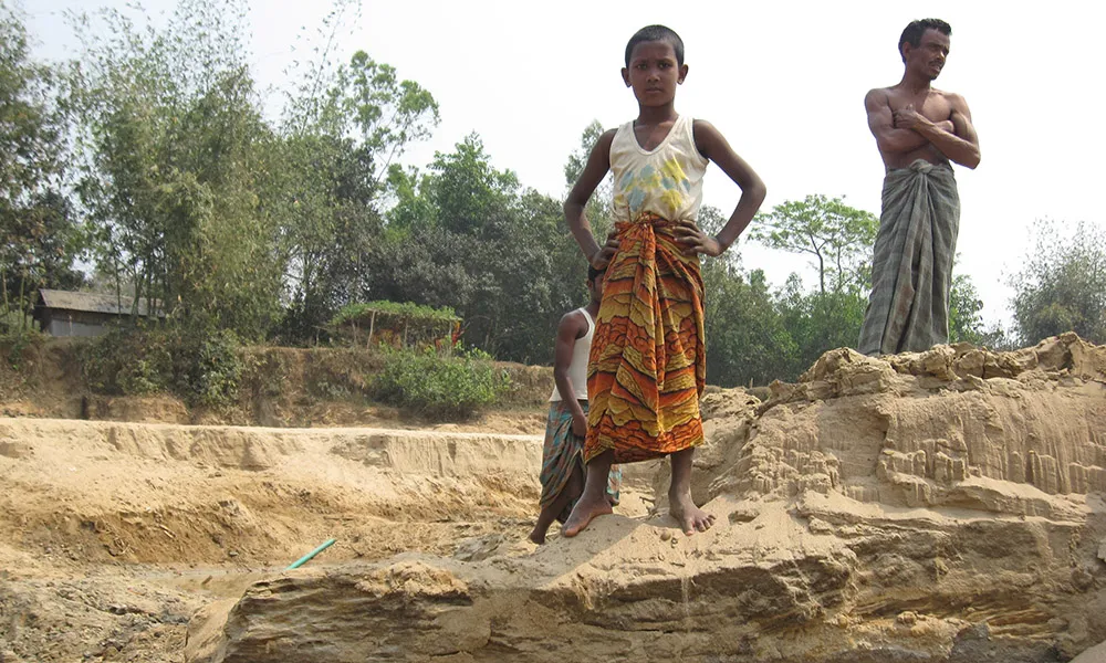 People who are unable to flee natural disasters and areas of high climate risk are vulnerable, and understudied. Here, a man and boy are surveying a dried-up riverbed in northern Bangladesh.  Photo credit: Kevin Krajick.